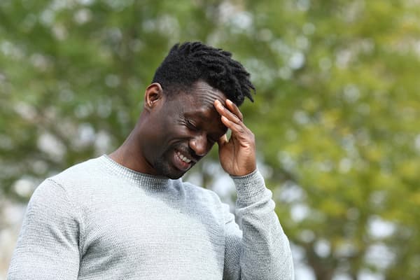 Black man standing with hand on his head and a face full of pain.
